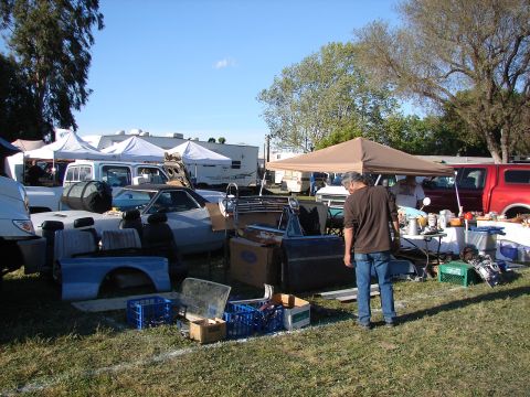 1973 Ford Ranchero - A variety of car parts and vehicles are displayed at an outdoor swap meet under a clear blue sky.