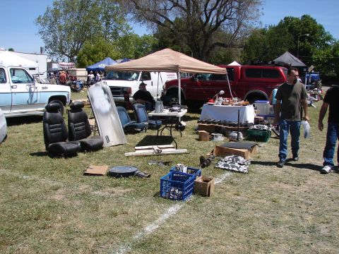1973 Ford Ranchero - Various car parts, including seats, are displayed on the grass at an outdoor event with multiple vehicles visible.
