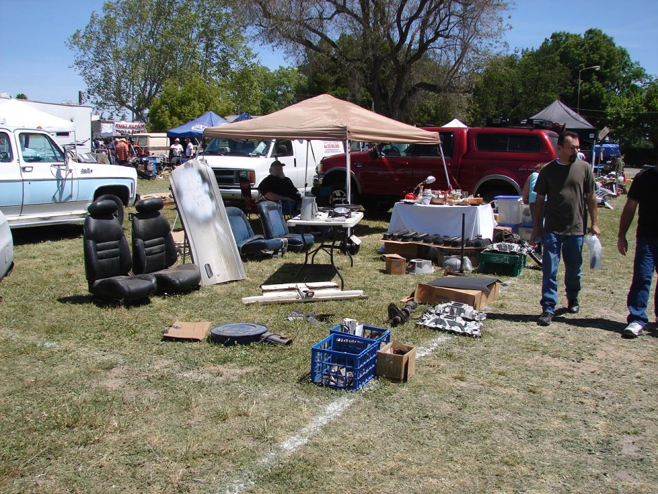 Car seats and parts laid out on grass with vehicles in background