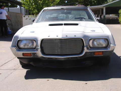 1973 Ford Ranchero - Front three-quarter-low head-on shot of a dusty white 1970s Ford with a horizontal-bar billet grille, chrome headlight bezels around dual r…