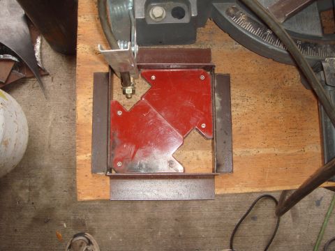 1992 Ford Bronco - Overhead shot of a fabrication setup on a plywood-topped bench: two red arrow-shaped magnetic welding squares holding four pieces of angle…
