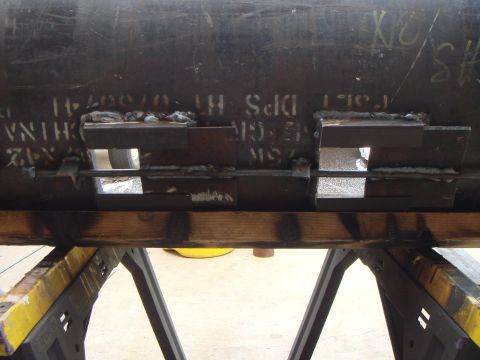 1992 Ford Bronco - A large steel pipe or tank section, still bearing white mill stencil markings including "CHINA," rests upside down on a wooden beam across…