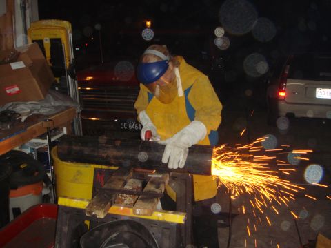 1992 Ford Bronco - A person in a yellow leather welding jacket, gloves and blue face shield angle-grinds a length of black steel pipe in a garage at night, th…