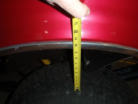 1995 Ford Bronco - A tape measure is used to measure the clearance between the fender and tire of a red vehicle.