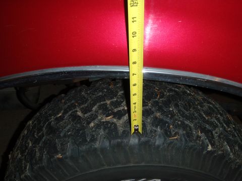1995 Ford Bronco - A tape measure is used to show the clearance between the tire and the fender of a red vehicle.