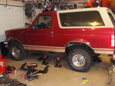 1995 Ford Bronco - This red Ford Bronco is parked in a garage with tools and jack stands around it.