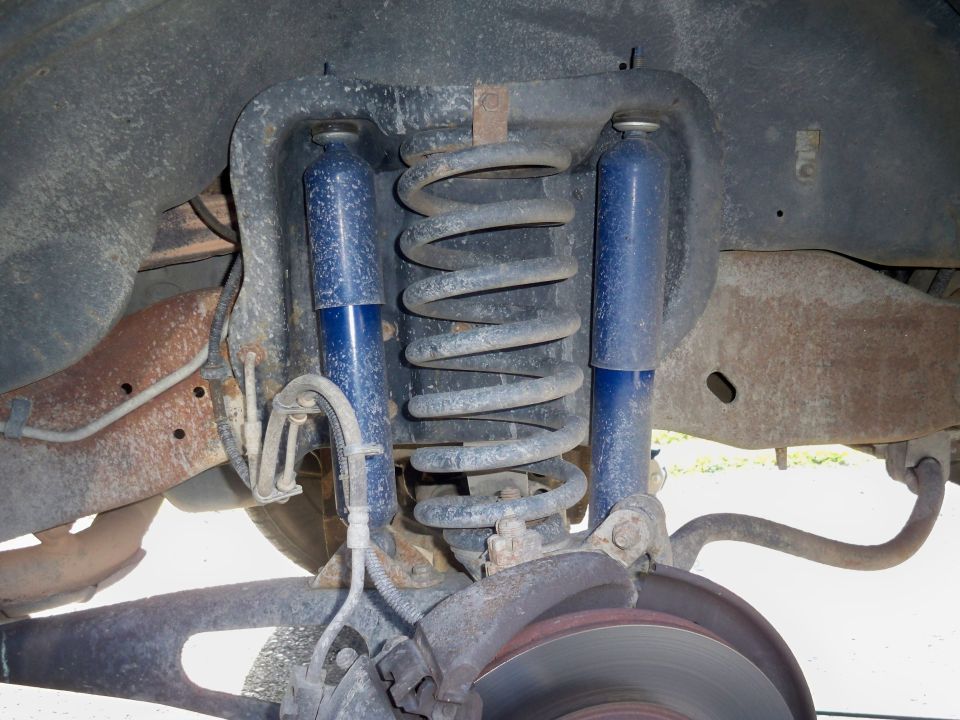 Front coil spring with dual blue shock absorbers and brake rotor under a truck chassis