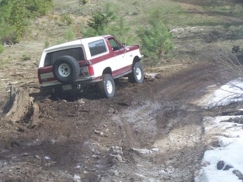 1991 Toyota Pickup/SR5 - A two-tone red and white Ford Bronco II navigates a challenging muddy terrain with snow patches visible.