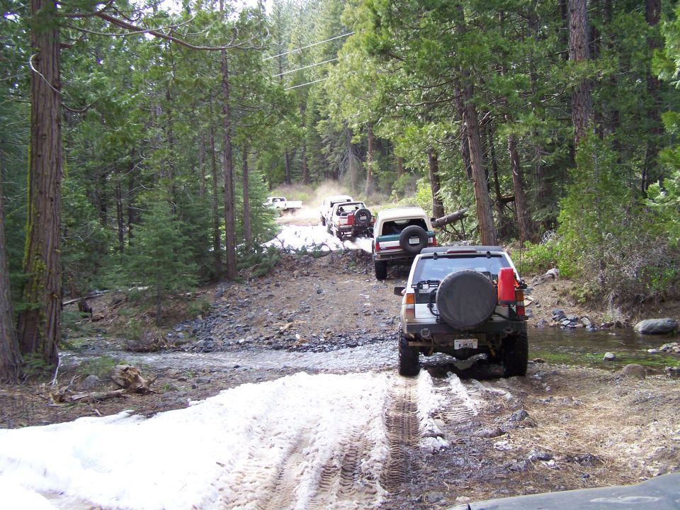 White Toyota 4Runner with spare tire on rear, driving on a snowy, muddy trail