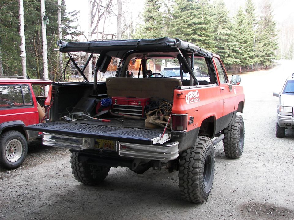 Orange lifted SUV with open tailgate, red Jeep Cherokee parked to the left, another vehicle to the right