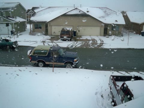 1994 Ford Bronco - A blue Ford Bronco is parked on a snowy street in front of a house.