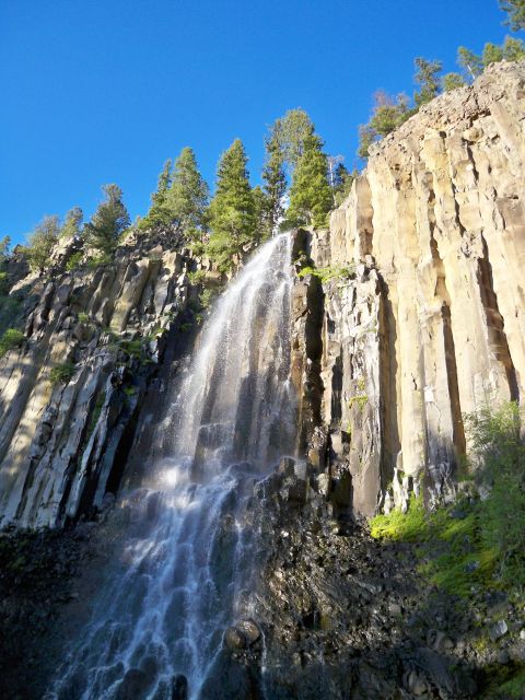 1994 Ford Bronco - Waterfall scene with columnar basalt cliffs and pine trees under a bright blue sky.