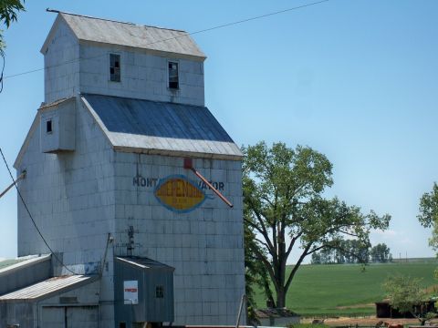1994 Ford Bronco - A weathered grain elevator stands tall against a clear blue sky, with a logo indicating it's a Montana Elevator.