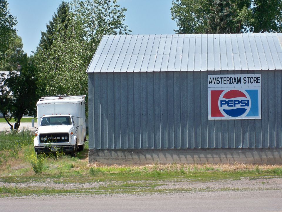 White box truck parked on grass next to a corrugated metal building with a Pepsi sign