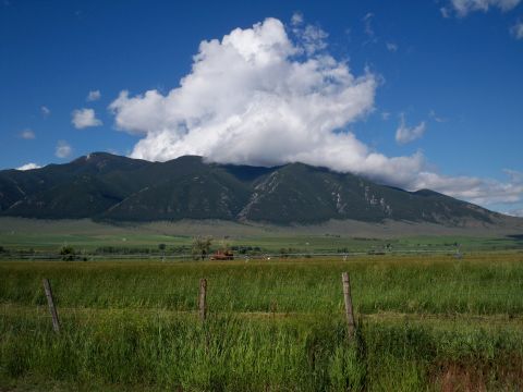 1994 Ford Bronco - A scenic view of a mountain range under a cloudy sky, with a field in the foreground and a SuperMotors logo at the bottom right.