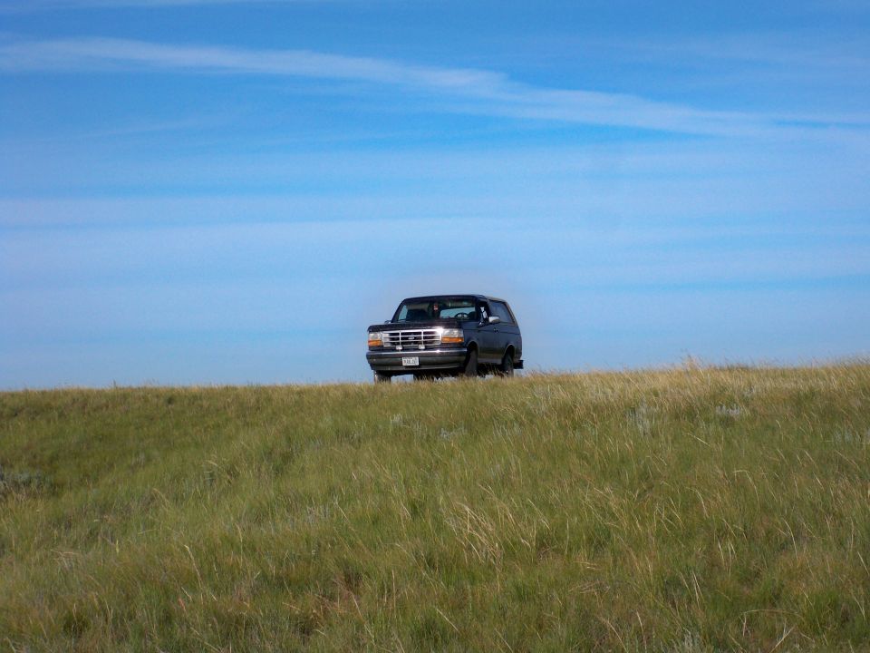 Dark SUV on grassy hill under blue sky