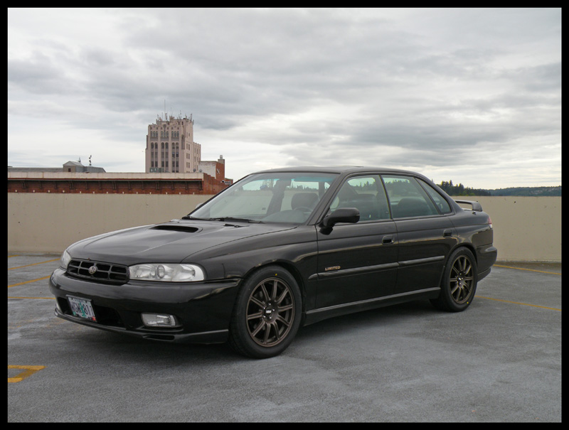 Black Subaru sedan parked on a rooftop with a building in the background