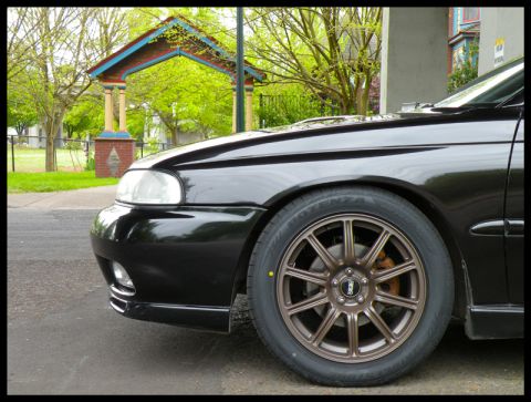 1998 Subaru Legacy - Bronze BBS wheels with orange brake calipers are visible on the front of a black car.