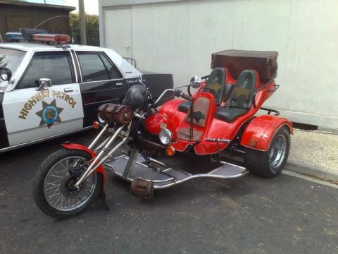 1991 Ford Crown Victoria - A custom red trike motorcycle is parked beside a black and white highway patrol car.