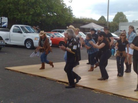 1991 Ford Crown Victoria - An outdoor event features people line dancing with cars visible in the background.