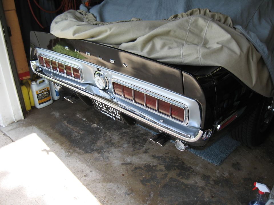 Rear of a 1968 Shelby GT500 with taillights and Shelby badging visible. Car is partially covered and parked in a garage