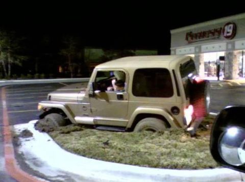 1989 Ford Bronco - A Jeep is stuck in the grass outside a Fitness 19 gym at night.