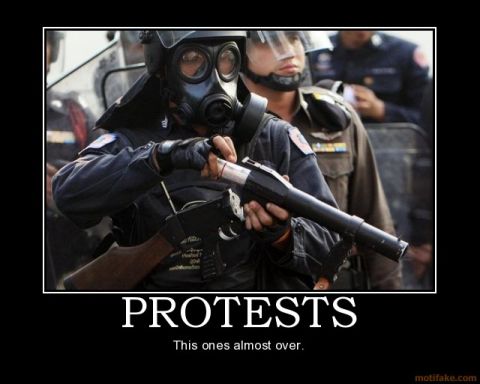 1989 Ford Bronco - A riot police officer wearing a gas mask and holding a weapon stands with other officers during a protest.