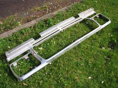 1979 Ford Bronco - A chrome grille assembly lies on a grassy area next to a paved surface.