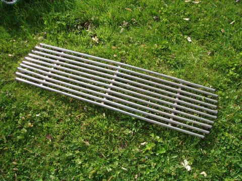 1979 Ford Bronco - A chrome grille with horizontal bars lies on a grassy surface, with a SuperMotors watermark visible.