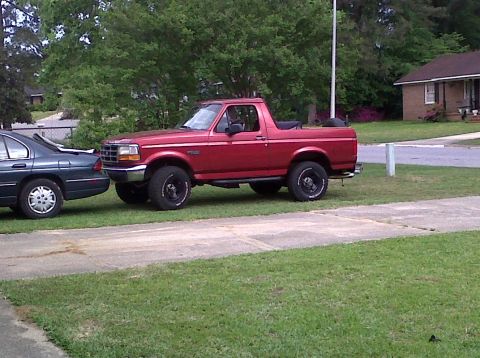1996 Ford Bronco - A red Ford Bronco is parked on a grassy area next to a dark sedan.