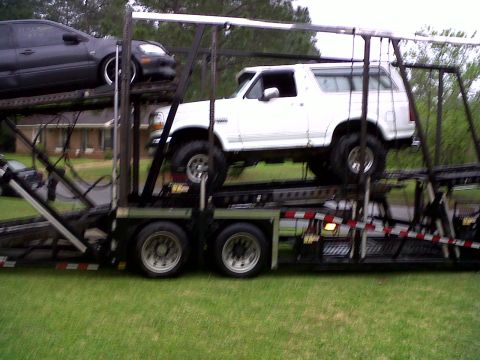 1996 Ford Bronco - White 1996 Ford Bronco being transported on a car hauler, with another vehicle above it.