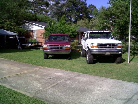 1996 Ford Bronco - A white 1996 Ford Bronco with a lifted suspension is parked on the grass next to a red pickup truck.