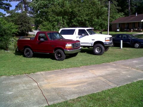 1996 Ford Bronco - 1996 Ford Bronco and a white SUV are parked on a grassy area next to a house.