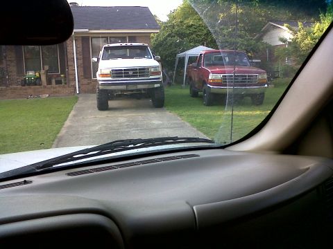 1996 Ford Bronco - Two Ford trucks are parked in a residential driveway, one white and one red.