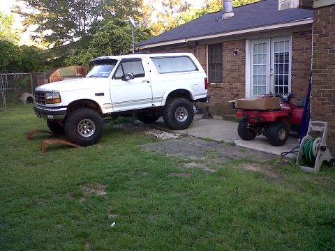 1996 Ford Bronco - A white Ford Bronco with aftermarket modifications sits in a residential backyard next to a brick house.