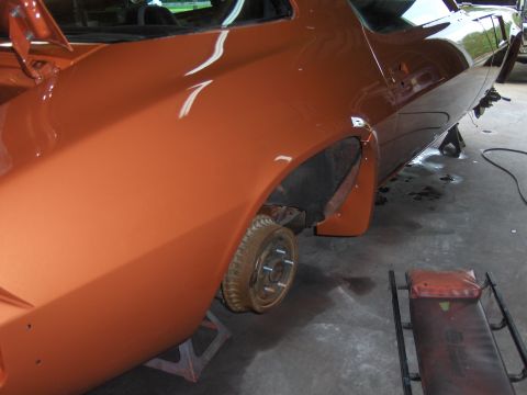 1980 Chevrolet Camaro - The rear quarter panel and wheel well of an orange car are visible while it is supported by jack stands.