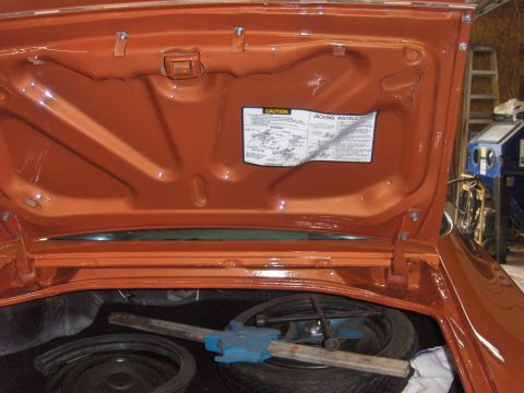 1980 Chevrolet Camaro - The trunk of an orange car is open, revealing a spare tire and jack, with a caution sticker on the lid.