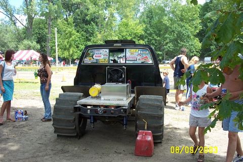 1996 Ford Bronco - A heavily modified truck with massive tires sits in a dirt lot, surrounded by onlookers.