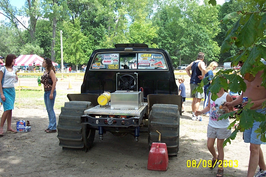 Black truck with oversized tires, exposed engine components, and a red gas can