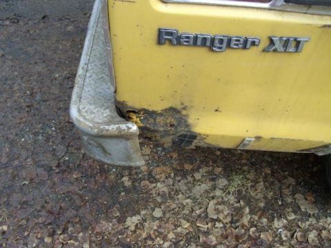 1976 Ford F-150 - The rear of a yellow 1976 Ford F-150 Ranger XLT shows significant rust damage and a damaged bumper.