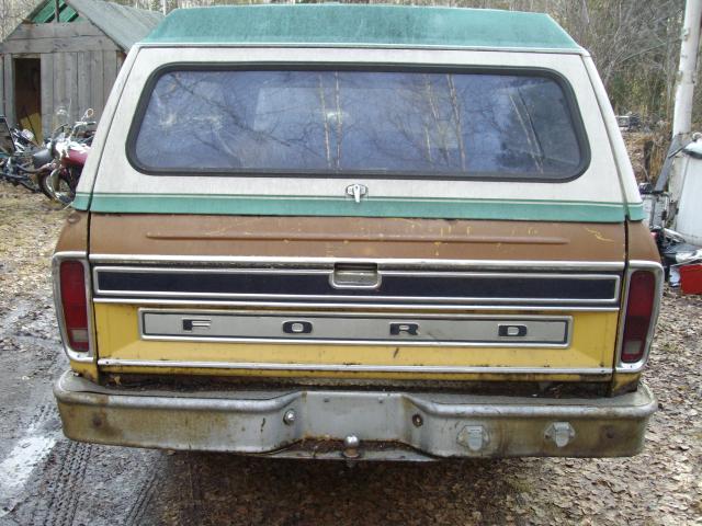Rear of a 1973 Ford F-150 pickup truck with a green camper shell, showing the tailgate with "FORD" lettering and a yellow and brown paint scheme