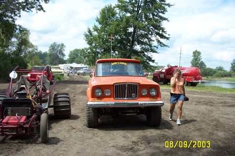 1996 Ford Bronco - An orange Jeep pickup truck is parked on a dirt path, with a dune buggy to its left and a woman walking past.