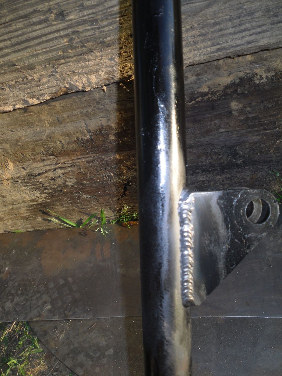 Close-up of a welded metal bracket attached to a black pipe, resting on weathered wood
