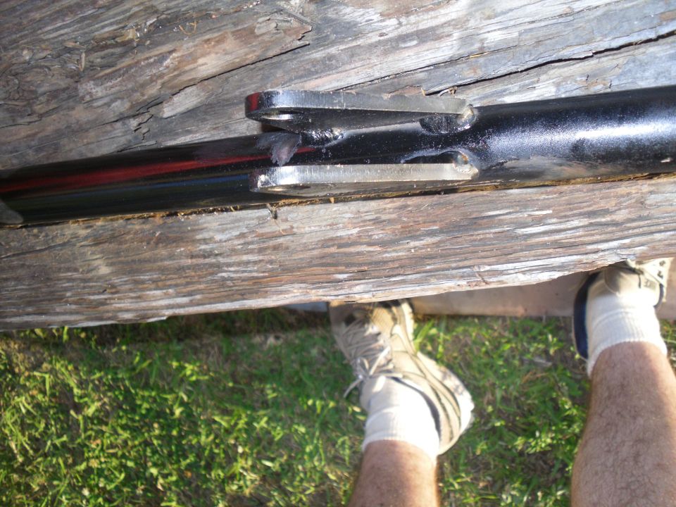 Black metal pipe with red stripe and two metal brackets attached, resting on wooden planks