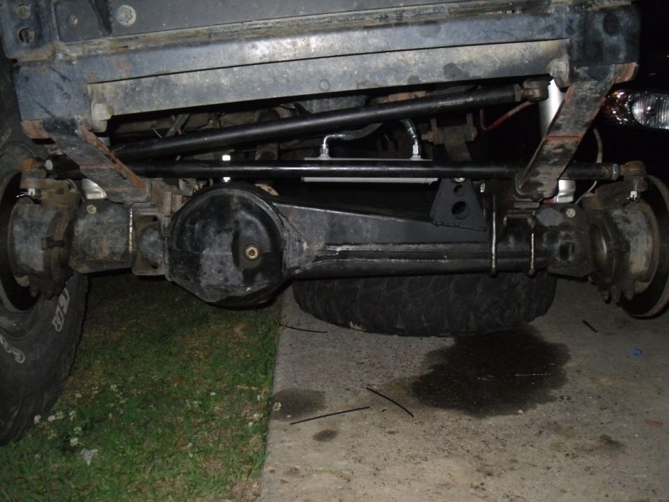 Rear axle, leaf springs, and shocks on a vehicle. Spare tire is visible underneath