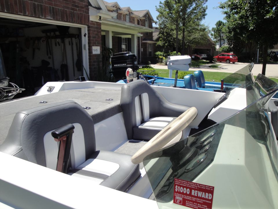 Bass boat cockpit with gray and white seats in a driveway, B.A.S.S. reward decal on windshield