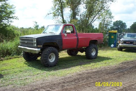 1996 Ford Bronco - This lifted pickup truck has a two-tone paint scheme and is parked outdoors with another vehicle and a portable toilet nearby.