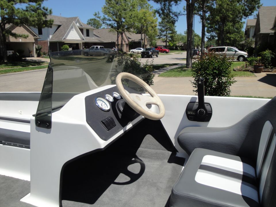 Boat helm with tan steering wheel, gauges, smoked windscreen and gray-white seats