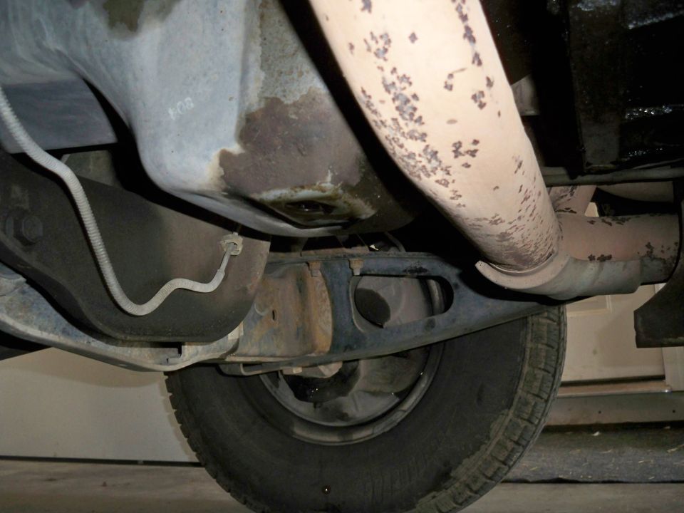 Underside of a vehicle showing exhaust pipe, oil pan, and tire