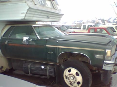 1994 Ford Bronco - A green pickup truck with a camper shell is parked outdoors among other vehicles.